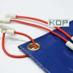 Blue tarp with a metal grommet, red 8″ or 12″ Scaffold Bungees with white plastic clips threaded through it. White object with "KOP" text partially visible in the background.