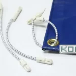 Blue tarpaulin with metal grommets, attached to plastic hooks by 8″ and 12″ Scaffold Bungees, and a printed label with the text "KOP" on the edge.