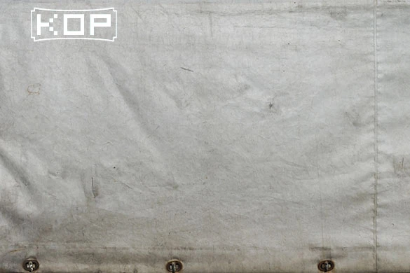 A close-up of a wrinkled white fabric with a "KGP" logo in the top left corner and metal grommets along the bottom edge.