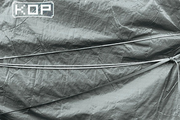 A tightly secured gray tarp with visible ropes spanning diagonally across its surface. "K:OP" is printed in the top-left corner.