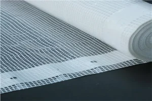 A roll of Clear String Reinforced Poly Tarps – 7 oz FR SCAFFOLD SHEETING is laying on a dark surface. The sheeting is partially unrolled, revealing its grid-like pattern.