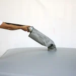 A person in a white shirt is shown inserting a gray hose into an opening on a gray Cube collapsible water tank with round corner reinforcement.