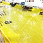 Several people are working with large sheets of Custom Printed Tarps, branded with "HESLY" logos, inside a well-lit industrial space.