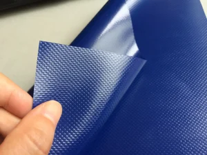 Hand holding a piece of Heavy Duty Tarpaulin roll with a blue textured and shiny finish.