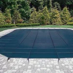 A rectangular swimming pool secured with a Safety swimming pool cover, surrounded by paving stones, and framed by neatly trimmed grass and bushes.