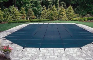 A rectangular swimming pool secured with a Safety swimming pool cover, surrounded by paving stones, and framed by neatly trimmed grass and bushes.