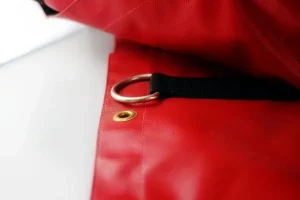 Close-up of the Lumber Tarp for Flatbed Truck and Trailer, showcasing its red fabric with a metal ring and black strap attached, alongside a brass grommet on a white background.