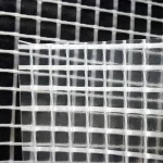 Close-up of FR SCAFFOLD SHEETING-10oz placed over a dark mesh background. The patterns of both meshes overlap, creating a grid effect with various shades of black, white, and grey.