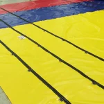 Close-up view of a large, colorful Lumber Tarp with Flap for Flatbed Truck and Trailer – 8′ Drop, divided into sections of yellow, blue, and red, with black straps laid across its surface.