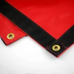 Close-up of a Lumber Tarp with Flap for Flatbed Truck and Trailer – 8′ Drop, featuring a red surface with black reinforced edges and brass grommets at the corners, laid out on a white surface.
