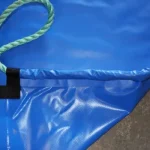 A close-up of a Snow Tarp corner with a green rope attached through a reinforced loop, lying on a concrete surface.